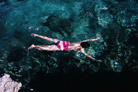 A wide shot of a person wearing pink and white swimsuit swimming in a clear seaの写真素材