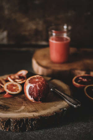 A vertical shot of a half peeled blood orange near a knife on a round wooden slab with a blurred backgroundの写真素材