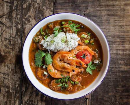 An overhead shot of soup with shrimp and vegetable leaves in a bowl on a wooden surfaceの写真素材