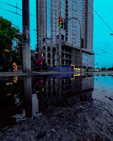 The reflection of a high building and the traffic light, and wires in the water on a damaged asphaltの写真素材
