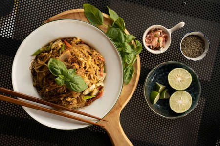 An overhead shot of a dish with noodles and vegetables near spices and lemonsの写真素材