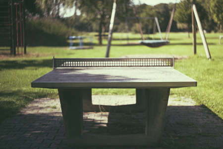 A stone tennis table in the park with a playground in the background on a sunny dayの写真素材