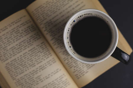 A high angle shot of a cup of coffee and an open book on the tableの写真素材