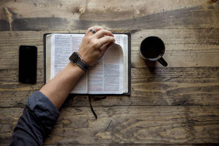 An overhead shot of a person flipping the page of a book near the coffee and a smartphone on a...