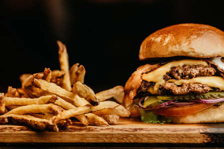 A closeup shot of a burger with bacon, cheese, pickles, onions, and tomato, fries next to the burger