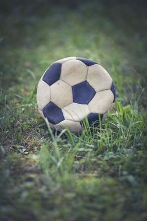 A vertical closeup shot of a worn-out soccer ball in a grassy fieldの写真素材
