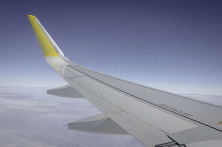 A closeup of the wing of a plane in the air under the sunlight and a blue skyの写真素材