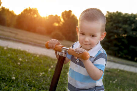 A closeup shot of a caucasian male child holding a scooter in the park during sunsetの写真素材