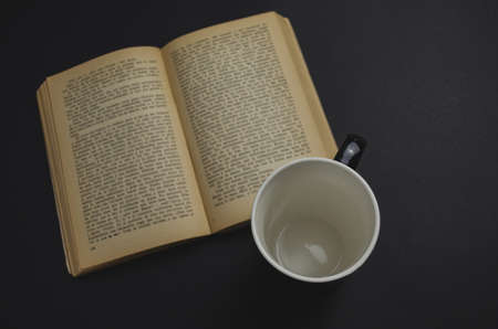 A high angle shot of an empty mug cup and an open book on the tableの写真素材