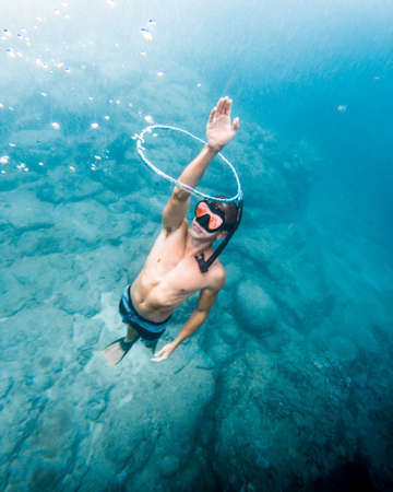 A vertical high angle shot of a male swimming underwater taking out his hand