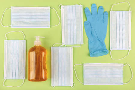 A high angle shot of a bottle of sanitizer, a glove and some surgical masks on a green surface