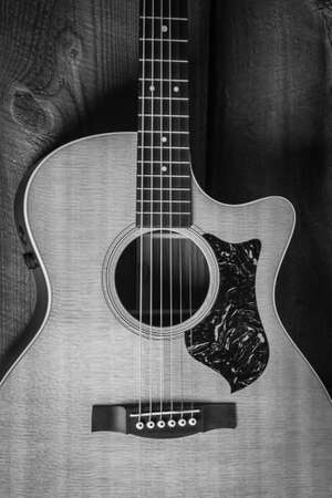 A beautiful grayscale shot of an acoustic guitar leaned on a wooden door on a wooden surface