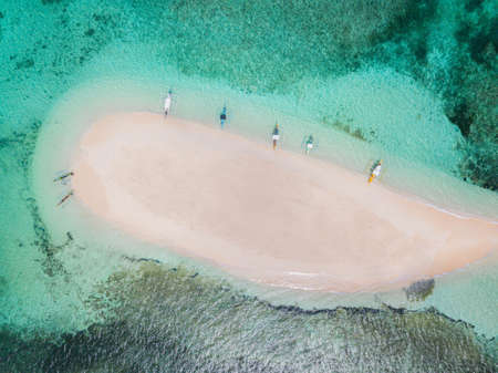 An aerial shot of a small sandy island surrounded by water with a few boatsの写真素材