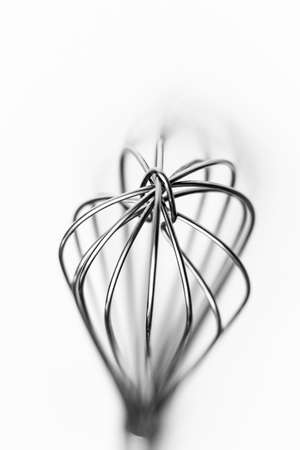 A selective closeup greyscale shot of whisks on a white background