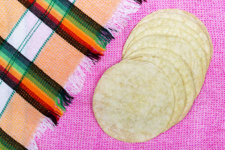 A high angle shot if several pieces of tortilla bread put on a pink surface next to a mexican cloth