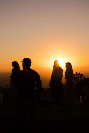 A vertical silhouette shot of people enjoying the beautiful view of the sunset on the top of a...
