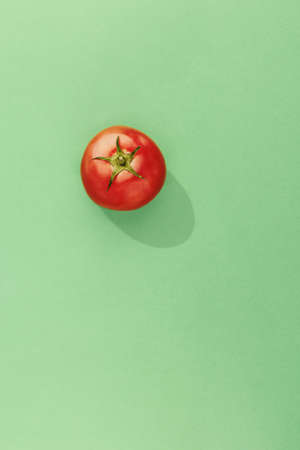 A vertical high angle shot of a fresh tomato isolated on a green surfaceの写真素材