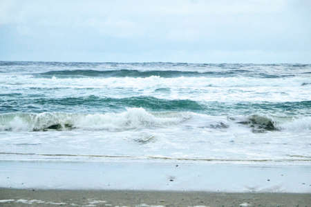 A horizontal shot of waves splashing on the beach during overcast