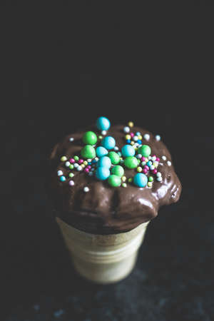 A vertical closeup shot of a chocolate ice-cream cone with sprinkles on a black background