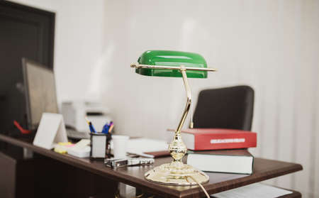 A closeup shot of a green desktop lamp at an office with books and filesの写真素材