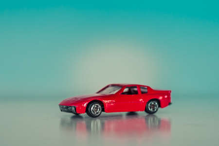A closeup shot of a decorative red toy car figurine with a reflection and on a light blue background