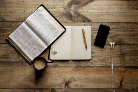 An overhead shot of a notebook with a fountain pen near an open book and smartphone on a wooden tableの写真素材