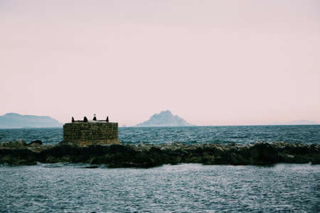 A beautiful shot of a sea with a small brick house in the middle and a clear sky in the backgroundの写真素材