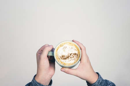 An overhead selective shot of a person holding a ceramic cup filled with latte art coffee on a white backgroundの写真素材
