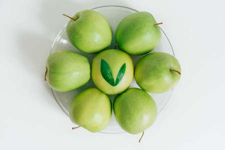 An overhead shot of green apples in a glass bowl with a white background