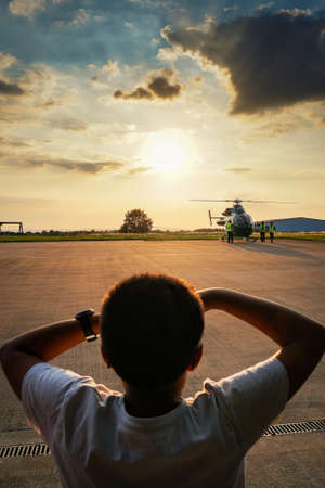 A vertical shot of beautiful large clouds in the sky and a young boy looking at the helicopter