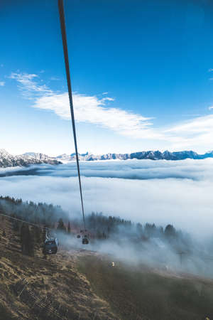 A high angle shot of ropeway wagons going towards the fog surrounded by high rocky mountainsの写真素材