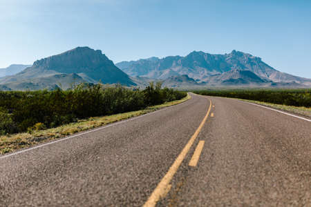 A beautiful shot of an empty road in the middle of plants and mountains in the distance with a clear...