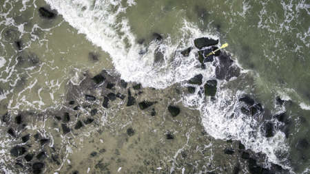 An aerial shot of green rocks on the beach under the beautiful waves of the ocean