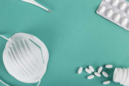 A high angle shot of a sanitary mask, a thermometer, and some pills on a blue surface - Pandemic