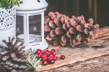 A closeup shot of red coffee beans and a pinecone with a candle lantern on a wooden surfaceの写真素材