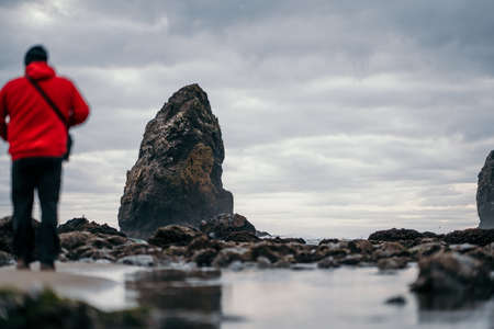 A beautiful shot of a male standing near a rock formation at the coast of the seaの写真素材