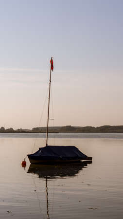 A vertical shot of a sailboat on the Rangsdorfer lake with gathered sails and covered with a tarp