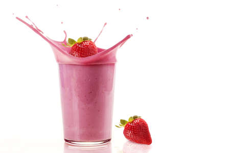 A closeup shot of a strawberry splashing the strawberry smoothie in a glass on a white backgroundの写真素材