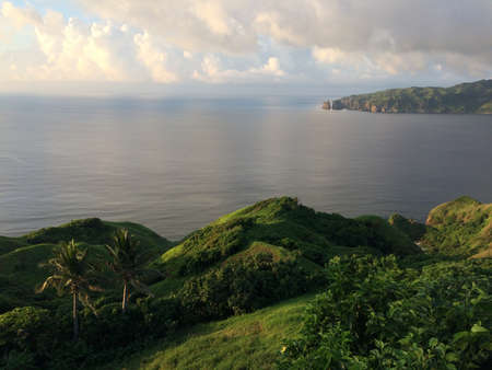 A beautiful wide shot of hills covered in green by the body of the sea under a cloudy sky