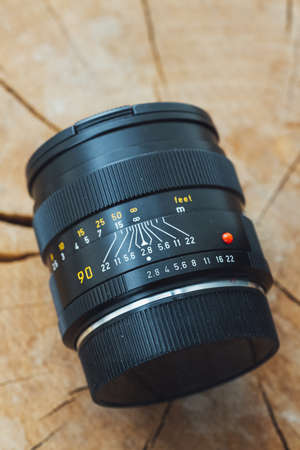 A vertical closeup shot of a professional camera lens on a wooden surface