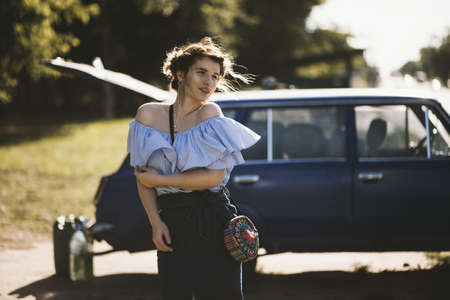 A shallow focus shot of an attractive female model in an off-shoulder dress posing near a vehicle