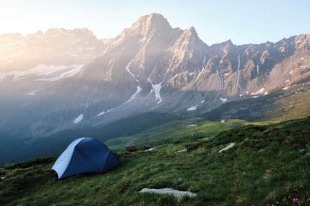 A beautiful shot of a blue tent on a grassy hill with mountains and clear sky in the backgroundの写真素材