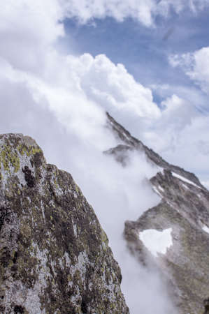 A vertical shot of rocky mountains covered in white clouds in a blue skyの写真素材