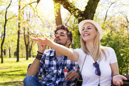 A happy caucasian couple sitting on a park bench, blowing bubbles and having funの写真素材