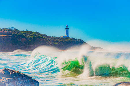 A beautiful shot of ocean waves and a beacon light tower on a cliff in the backgroundの写真素材