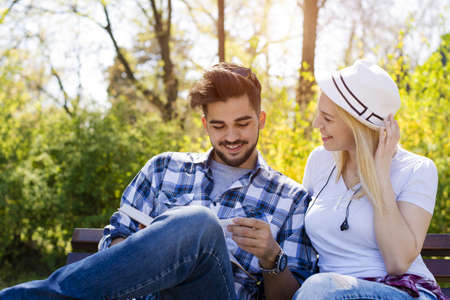 A happy caucasian couple sitting on a park bench, reading a book together