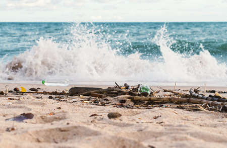 A selective focus of rubbish on the beach with big waves hitting the shore int he backgroundの写真素材