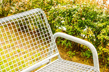 A closeup shot of a white metal bench in a park during the daytime