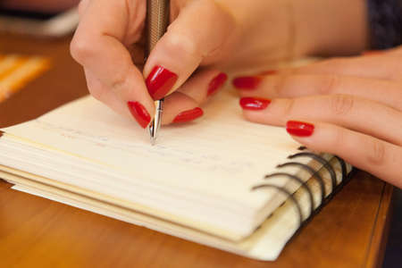 A closeup shot of a female's hand holding a pen and writing something in a textbookの写真素材