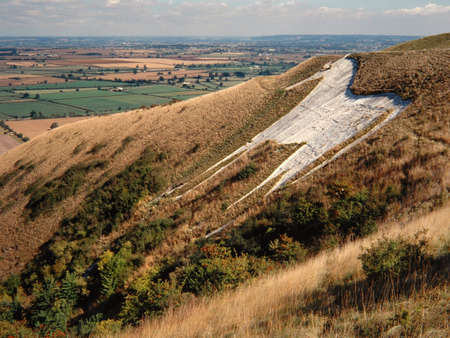 A wide shot of a hill covered with plants and a horse carving surrounded by flat grass fieldsの写真素材